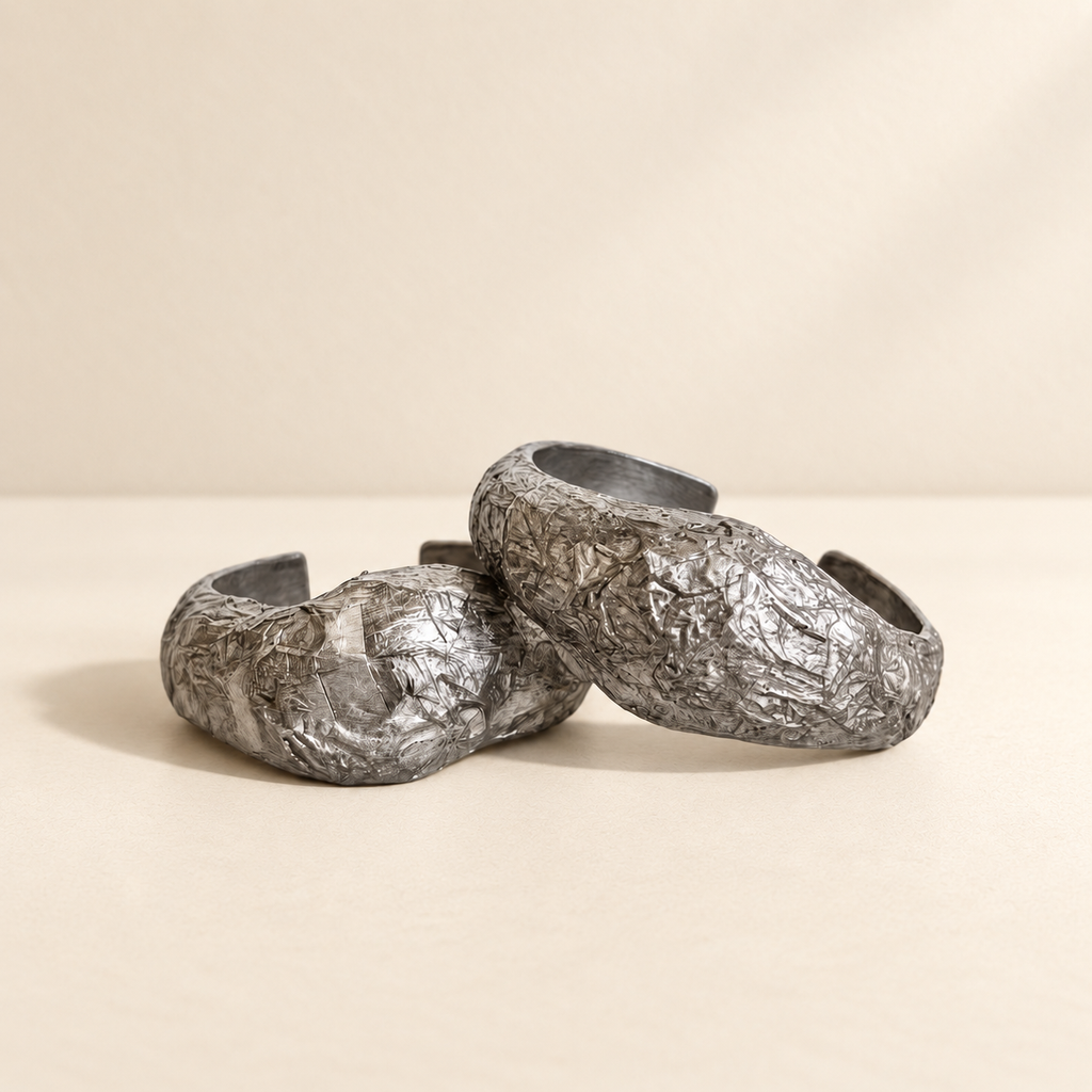Silver Strata — Sculptural Paper Cuff Bracelet resting on a warm ivory studio surface with a natural grounding shadow — Niksa Design