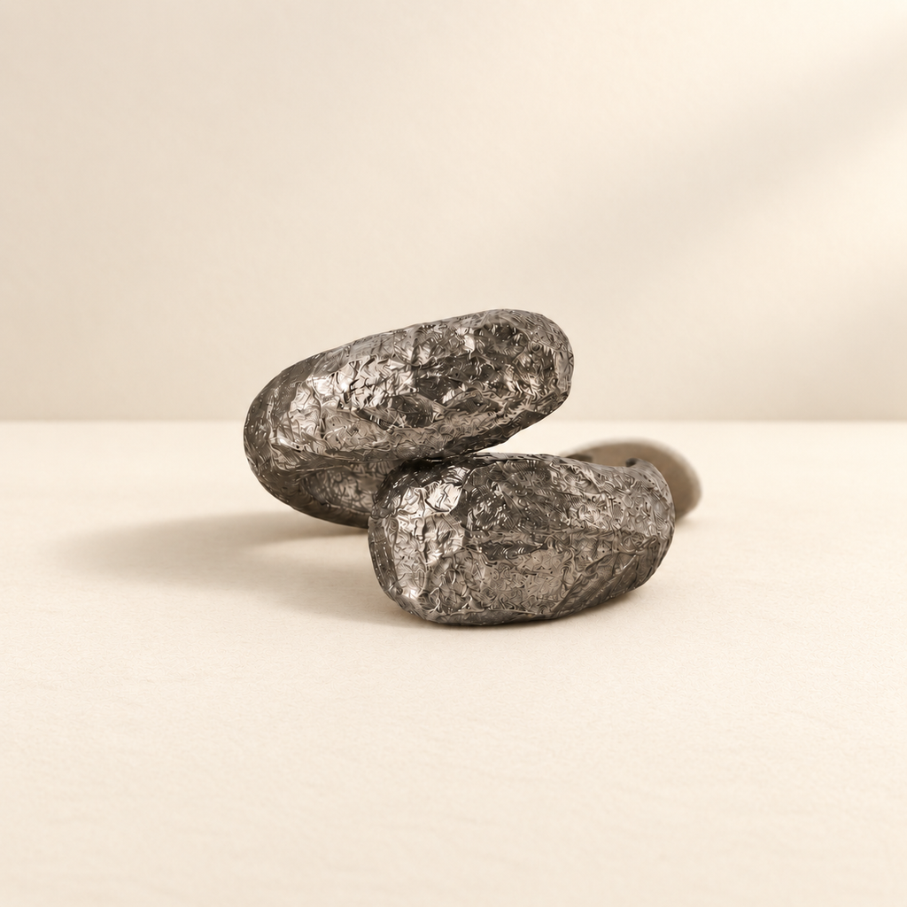 Held Orbit — Sculptural Paper Cuff Bracelet resting on a warm ivory studio surface with a natural grounding shadow — Niksa Design