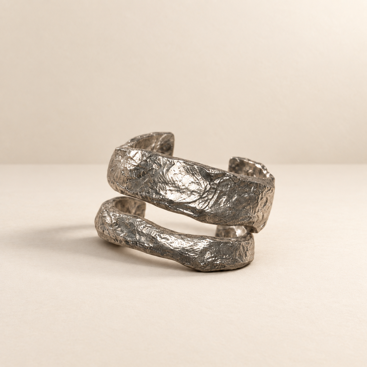 Crosscurrent sculptural paper cuff bracelet in a silver-toned finish on a warm ivory surface — Niksa Design