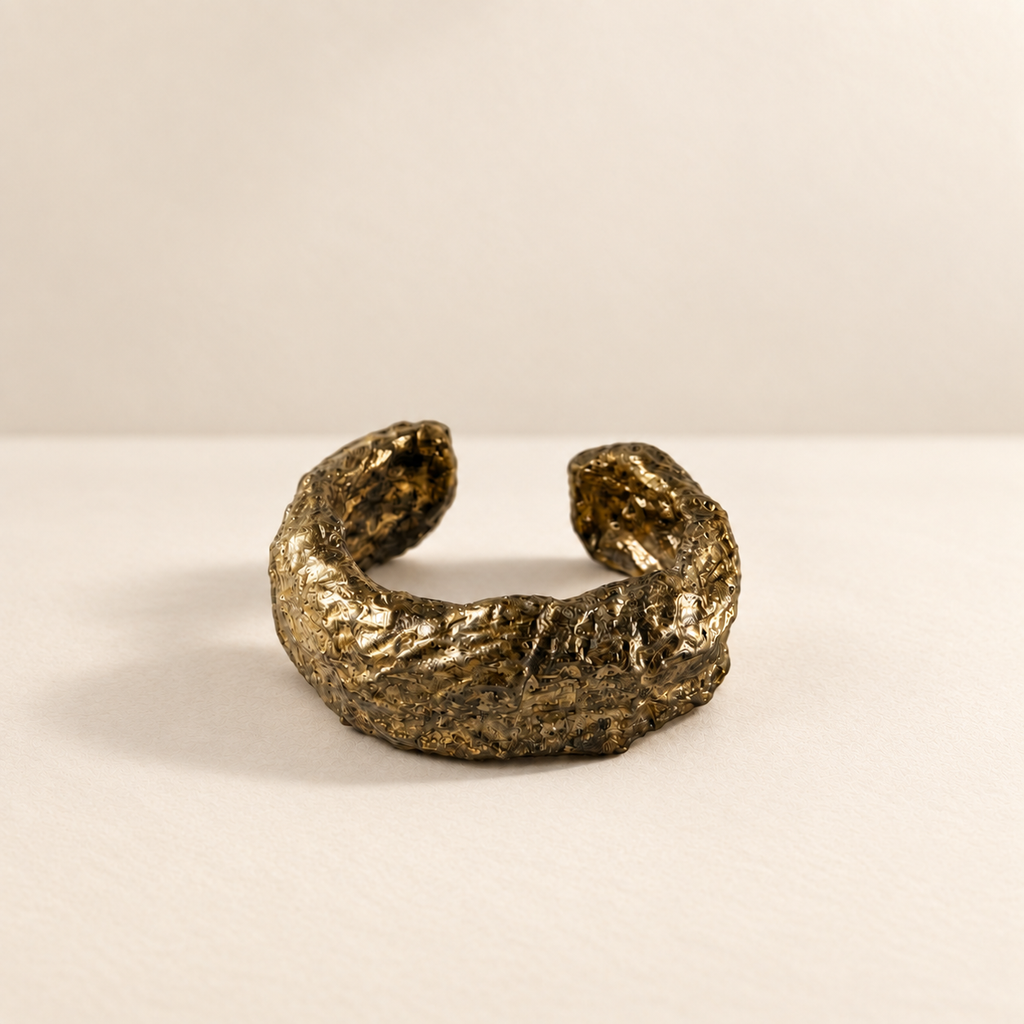 Gilded Seam — Sculptural Paper Cuff Bracelet resting on a warm ivory studio surface with a natural grounding shadow — Niksa Design