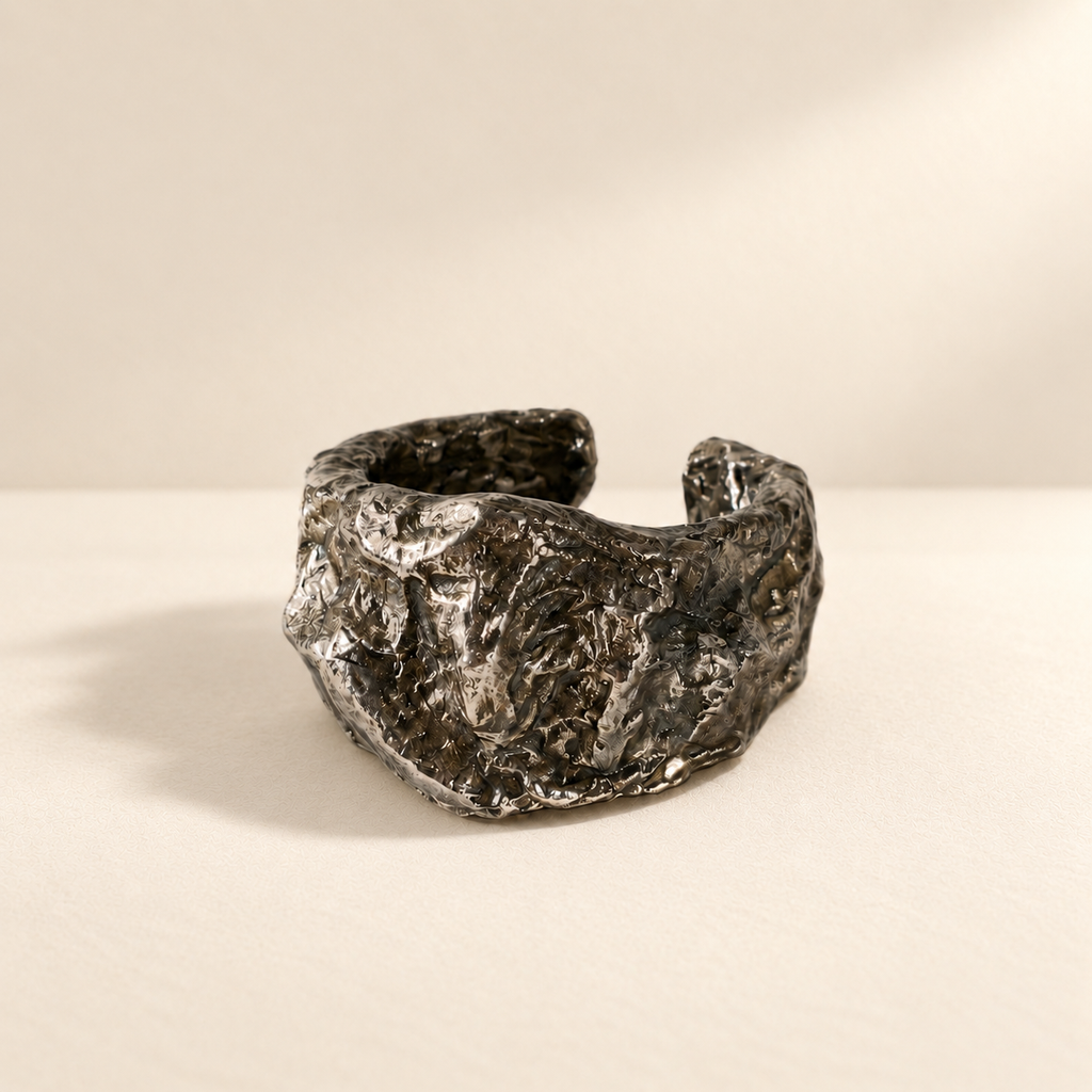Compressed Shield — Sculptural Paper Cuff Bracelet resting on a warm ivory studio surface with a natural grounding shadow — Niksa Design