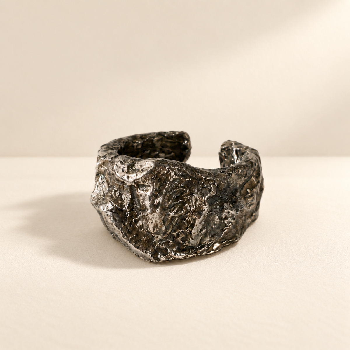 Compressed Shield — Sculptural Paper Cuff Bracelet resting on a warm ivory studio surface with a natural grounding shadow — Niksa Design