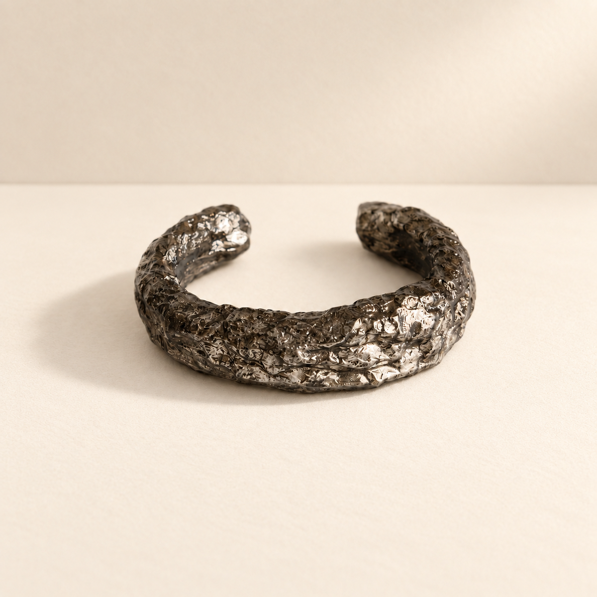 Silver Arc — Sculptural Paper Cuff Bracelet resting on a warm ivory studio surface with a natural grounding shadow — Niksa Design