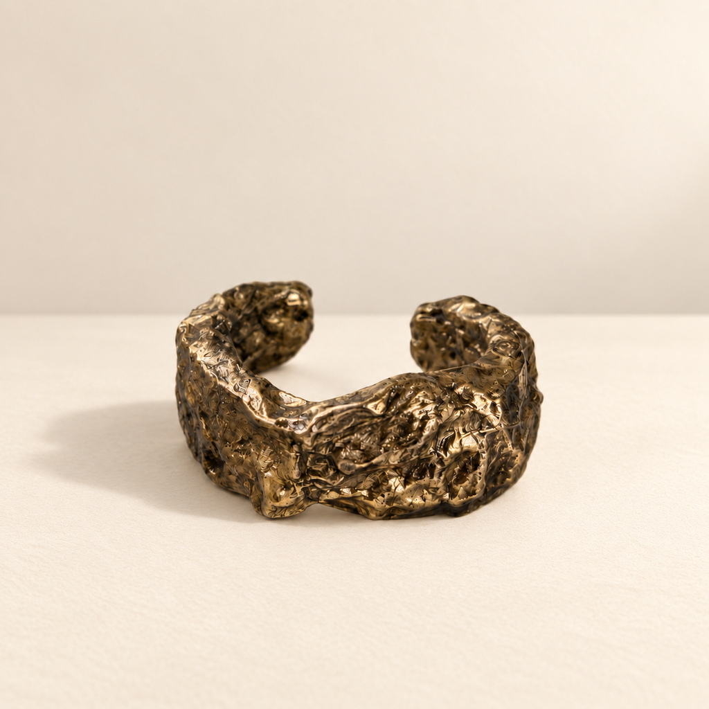Gilded Swell — Sculptural Paper Cuff Bracelet resting on a warm ivory studio surface with a natural grounding shadow — Niksa Design