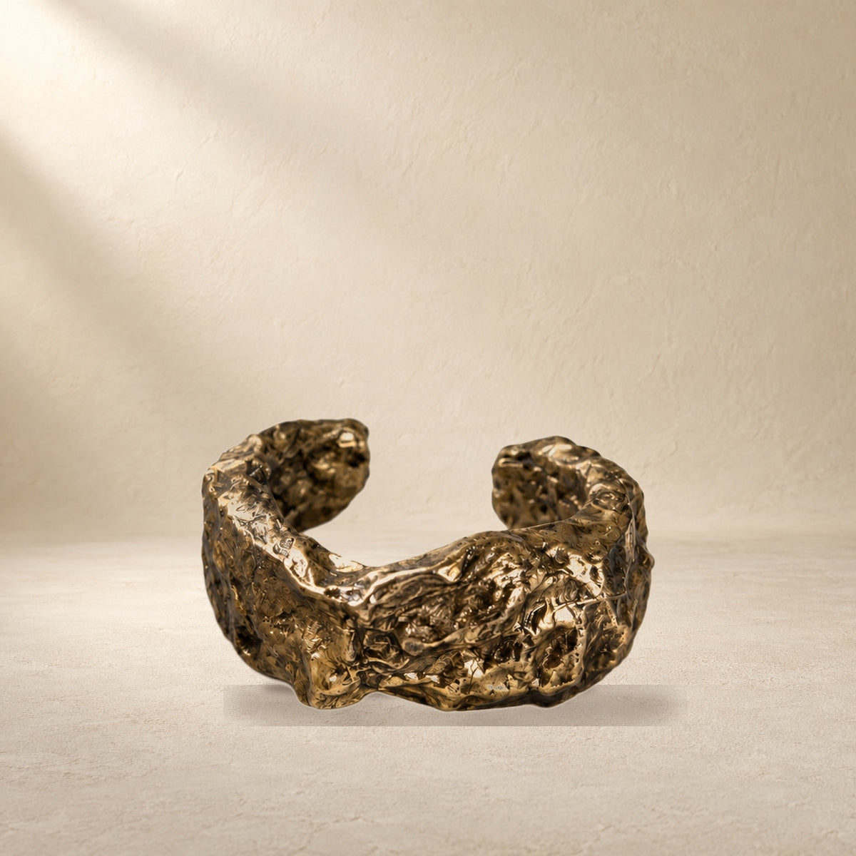 Gilded Swell bracelet resting on a warm cream surface