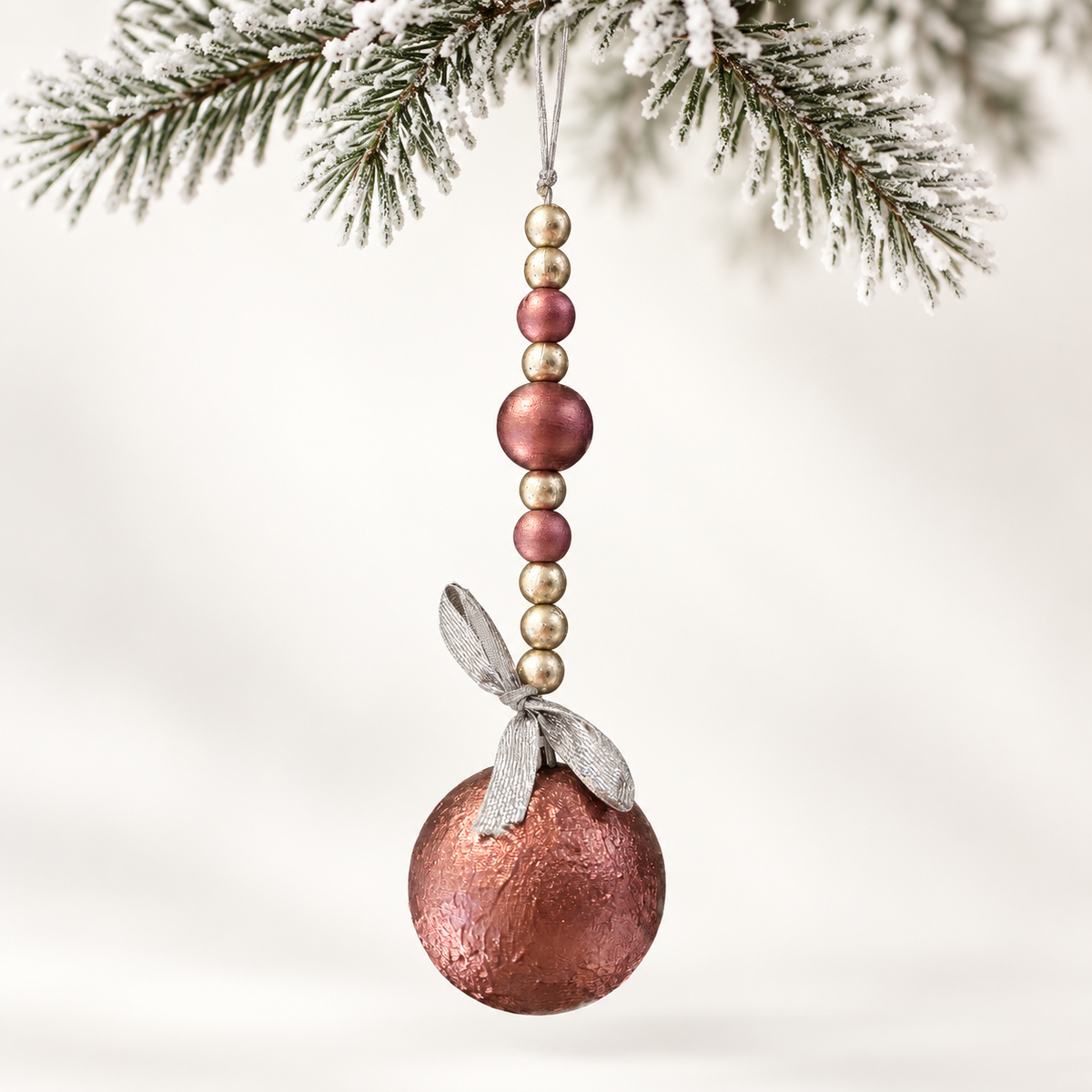 Rose copper-toned ball with a strand of rose and silver-toned beads and a silver ribbon.