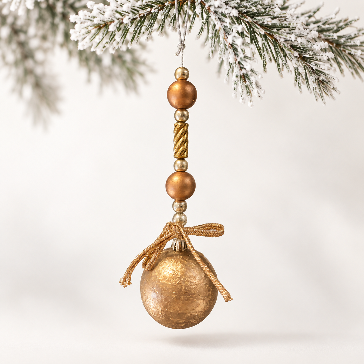 Gold-toned ball with metallic beads, a twisted centre bead and a gold-toned cord bow.