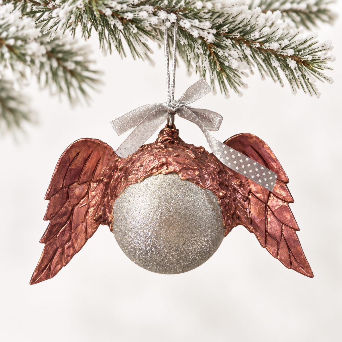A textured silver-toned sphere framed by copper-toned wings and a star-patterned ribbon.
