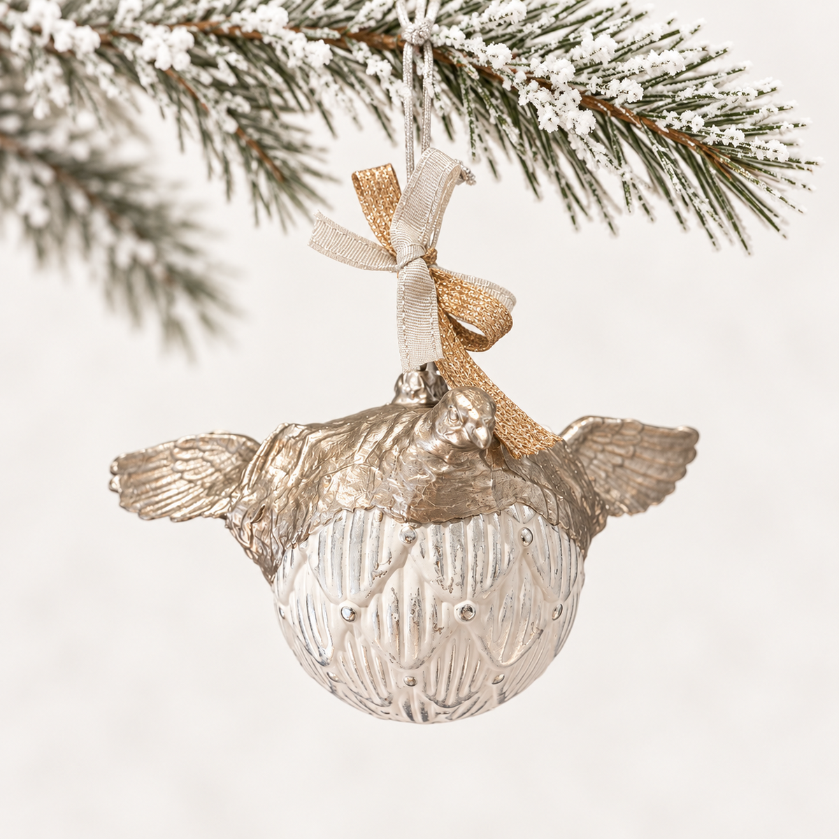 Silver-toned bird and outstretched wings above a patterned ivory sphere with silver and gold-toned ribbons.